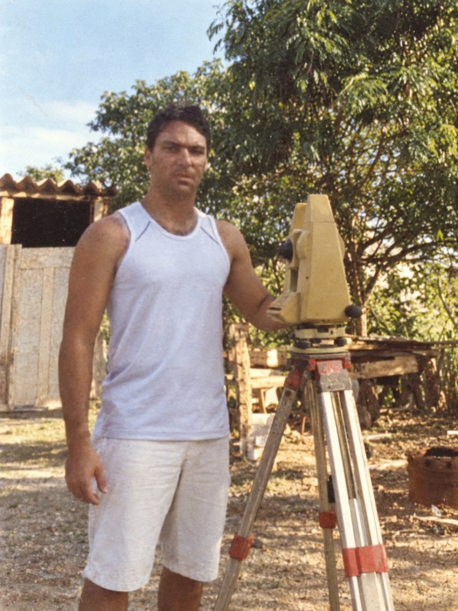 Registro histórico de 1999, no início da trajetória profissional em topografia, ao lado de um equipamento topográfico antigo